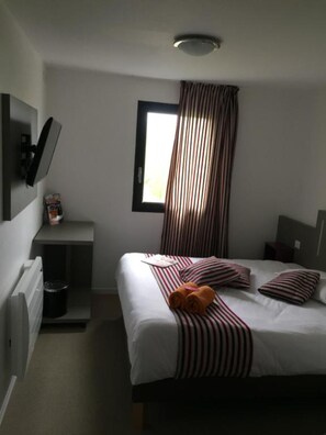 A hotel room with a bed, a TV mounted on the wall, a window with curtains, and a small table with a trash bin. - Kyriad Direct La Rochelle Sud Aytré (Aytre)