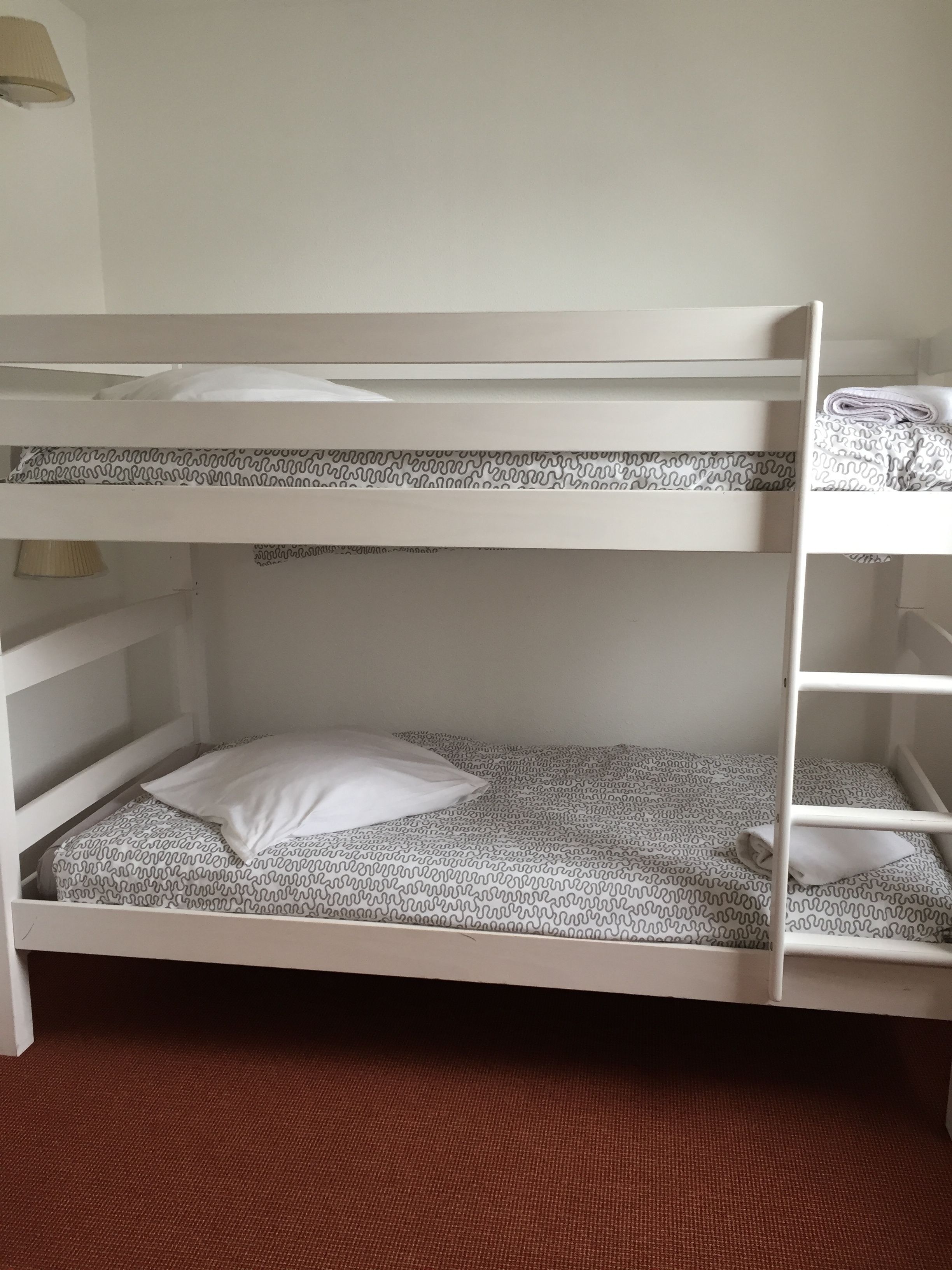 Een stapelbed met een beddengoed met patroon, een kussen en een klein plankje.