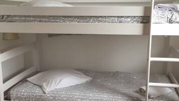 Een stapelbed met een beddengoed met patroon, een kussen en een klein plankje.