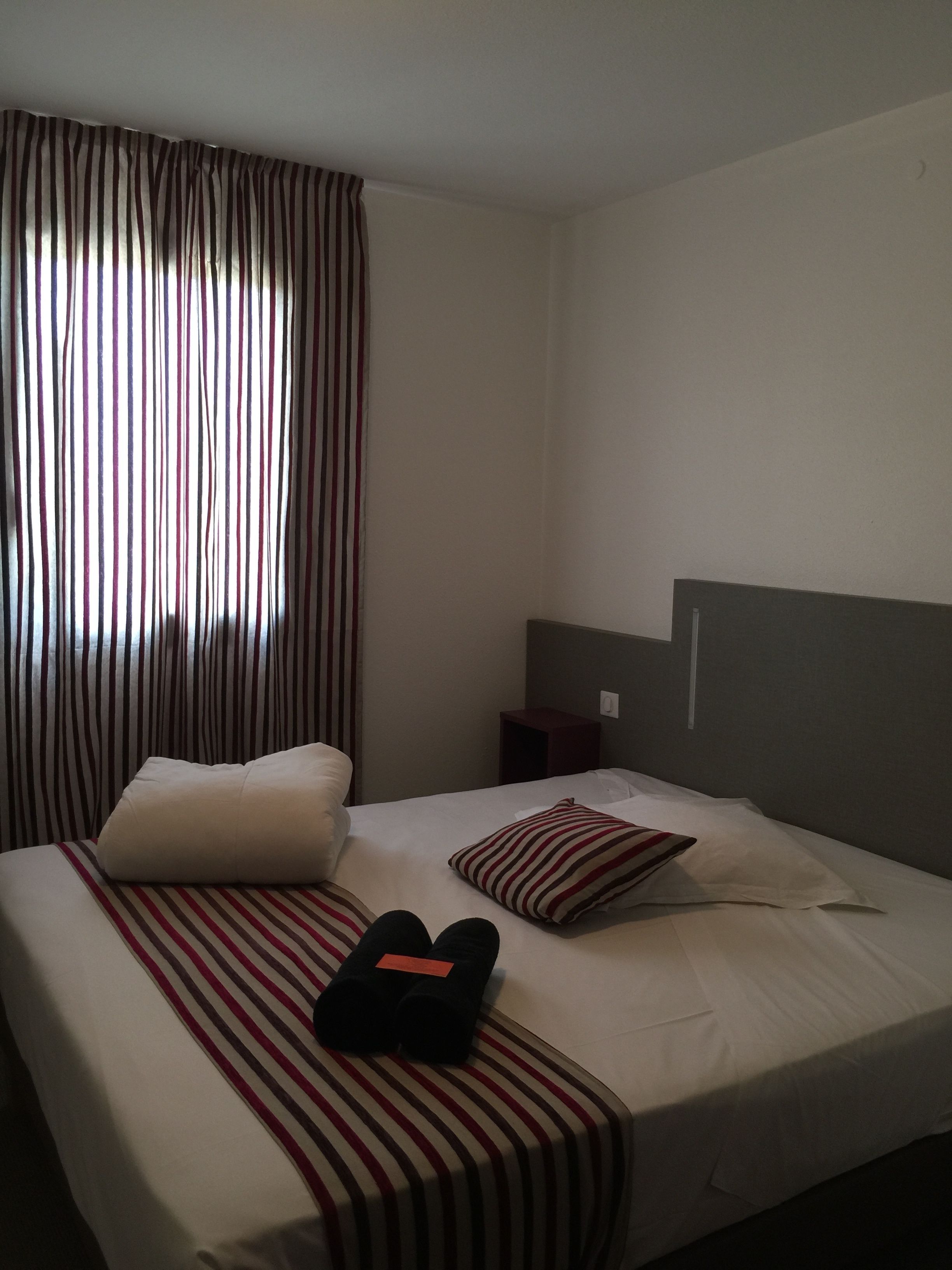 Hotellihuone, jossa on sänky, raidalliset verhot, yöpöytä ja sängynpääty.