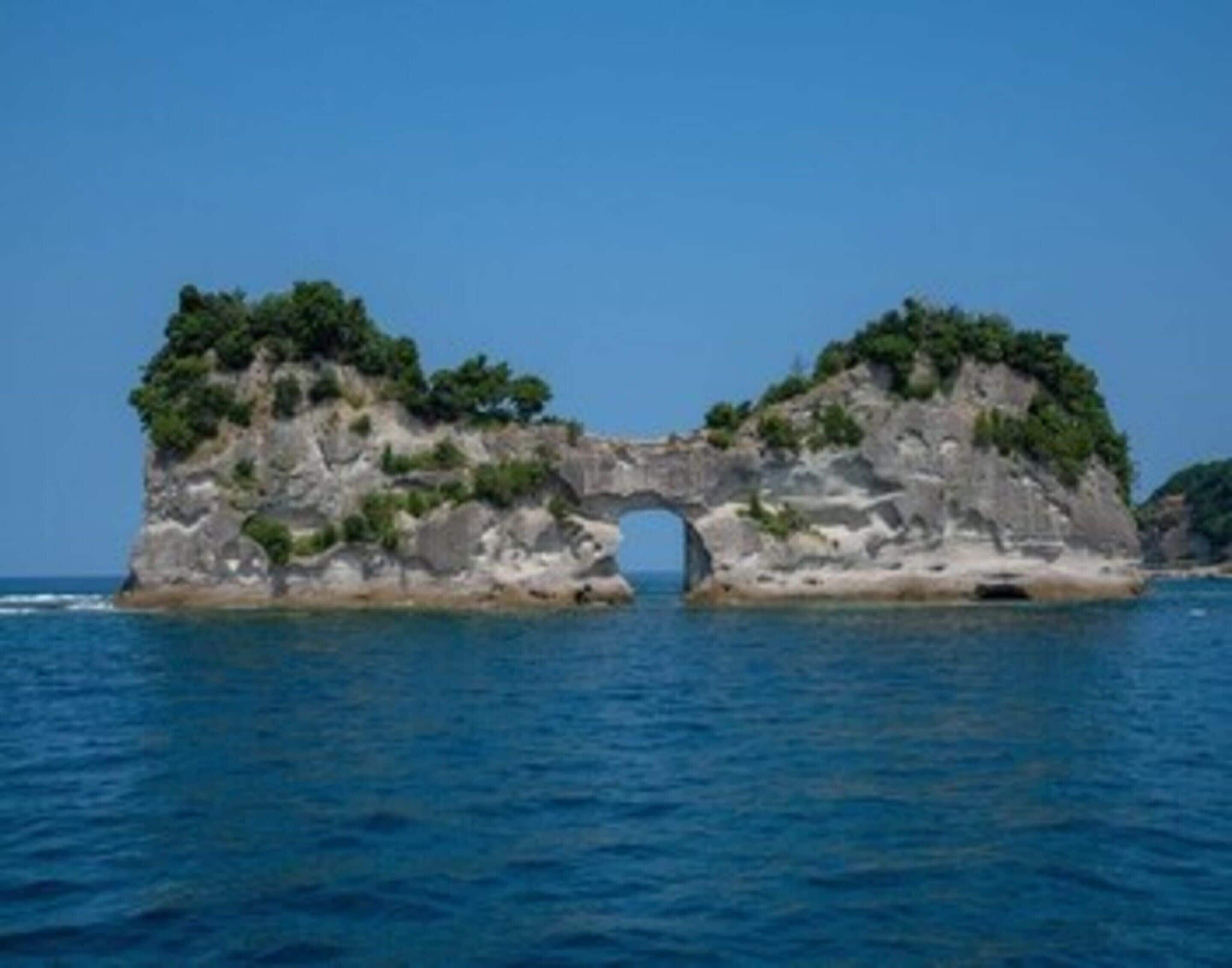 A natural rock formation with a large arch over a body of water.
