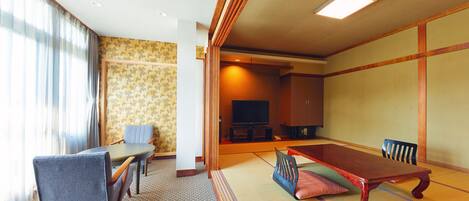 A traditional Japanese-style room with tatami flooring, a low table with cushions, a television, and a sofa.