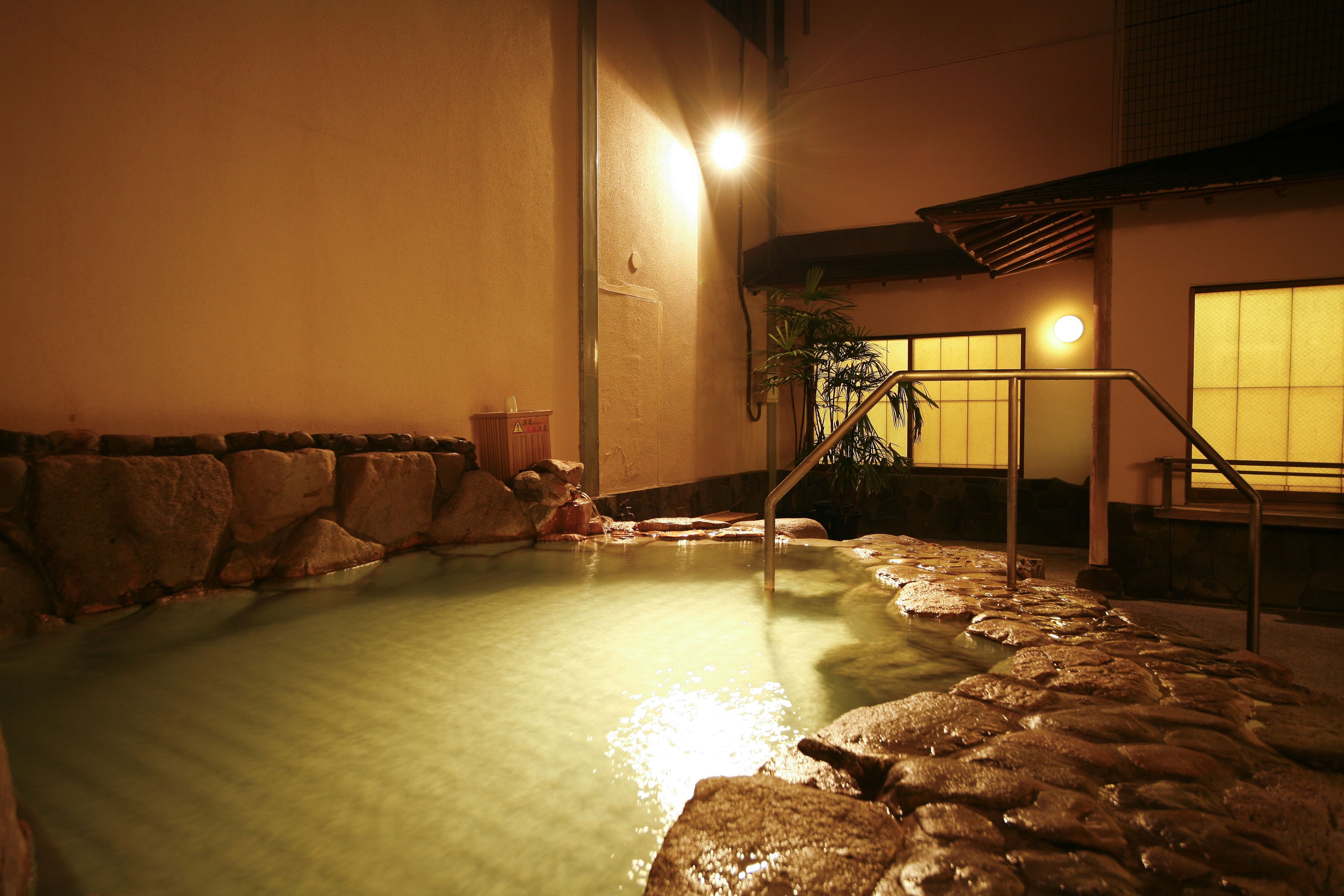 A hot spring area with a stone border, a wooden bench, and a staircase leading up.