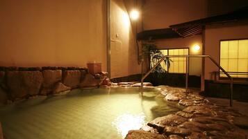 A hot spring area with a stone border, a wooden bench, and a staircase leading up.