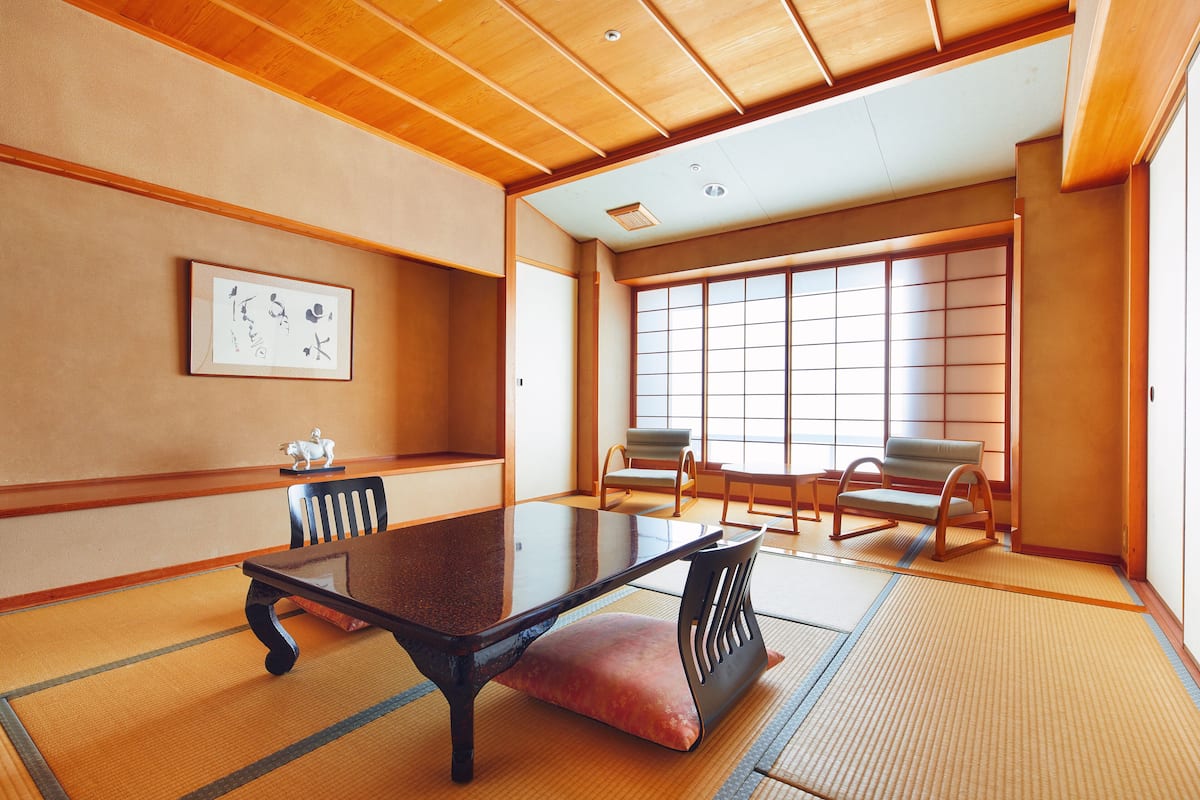 A traditional Japanese room with tatami flooring, a low table, and two chairs.