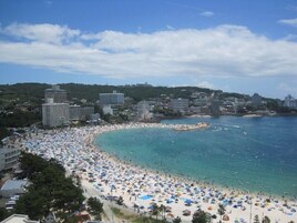 Una playa concurrida con numerosos sombrillas y gente, rodeada de edificios y colinas.