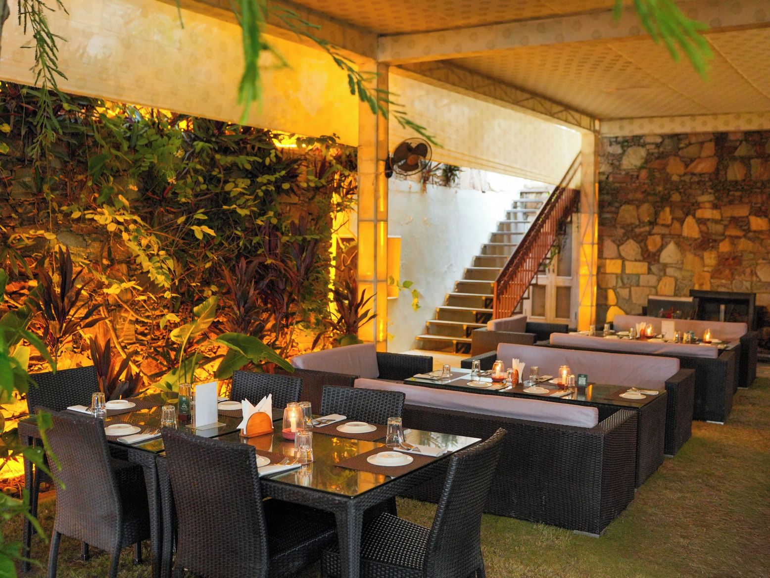 An outdoor dining area with wicker furniture, a stone wall, and a staircase.
