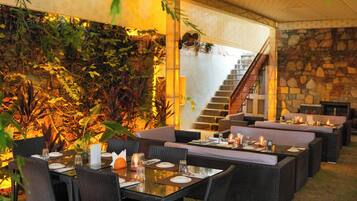 An outdoor dining area with wicker furniture, a stone wall, and a staircase.