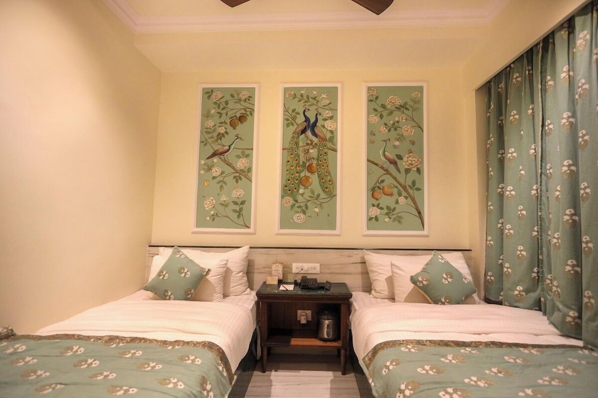 Une chambre d’hôtel avec deux lits, une table de chevet et un mur orné de trois tableaux floraux encadrés.