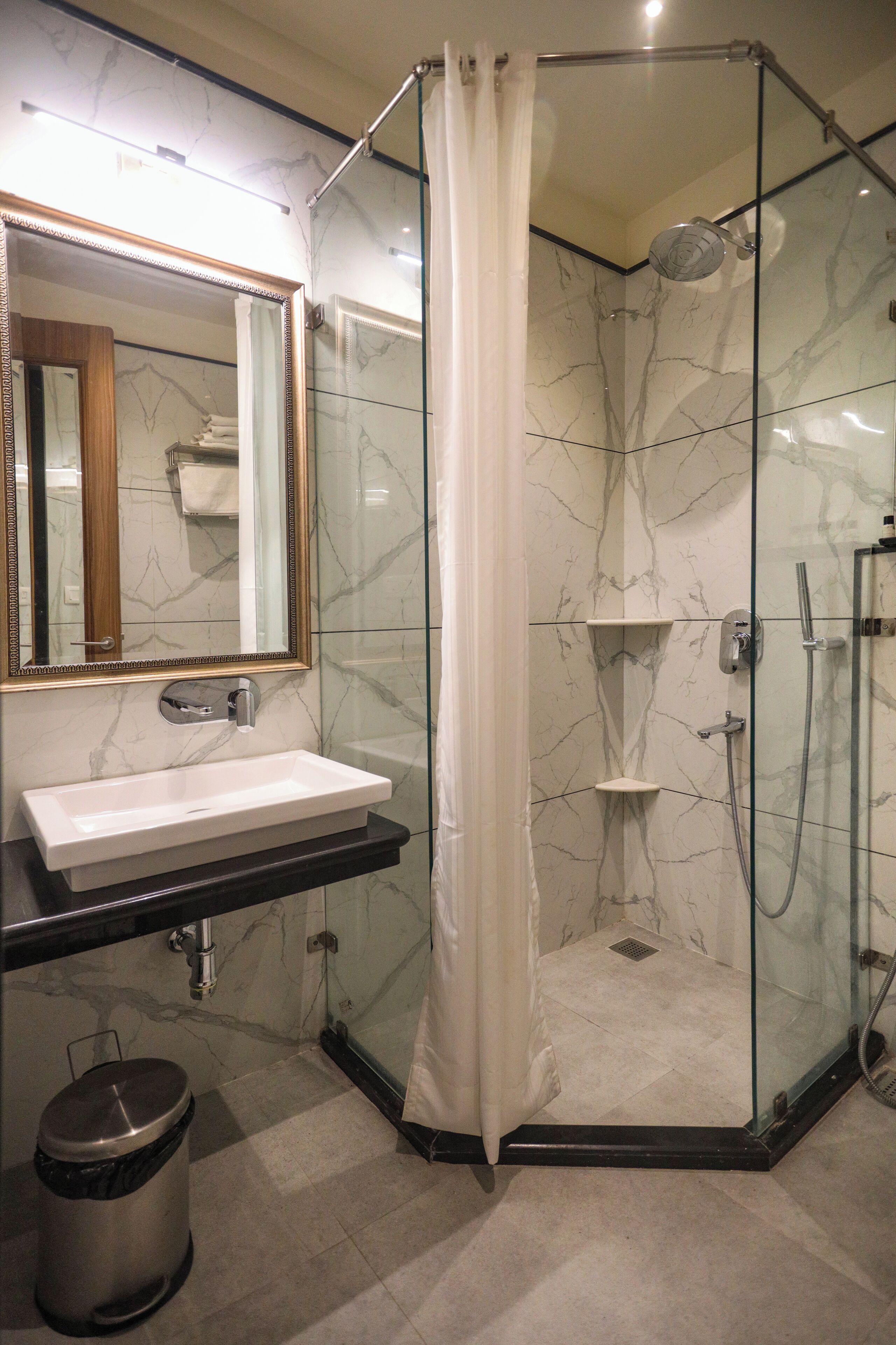 Une salle de bain moderne avec une douche en verre, un lavabo blanc et un mur recouvert de carreaux de marbre.