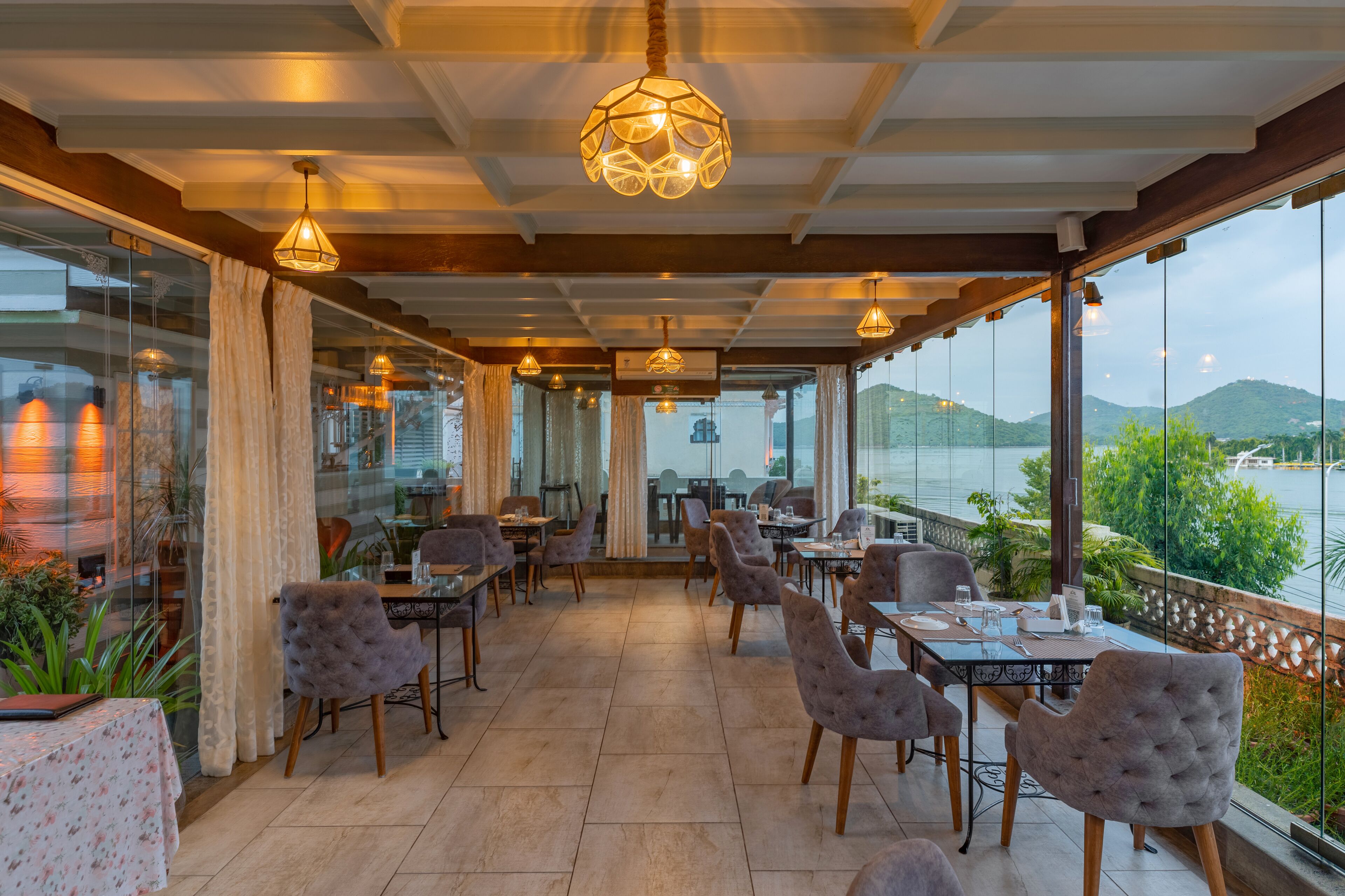 Restaurante com terraço voltado para um corpo d'água, com mesas e cadeiras, e luminárias pendentes.