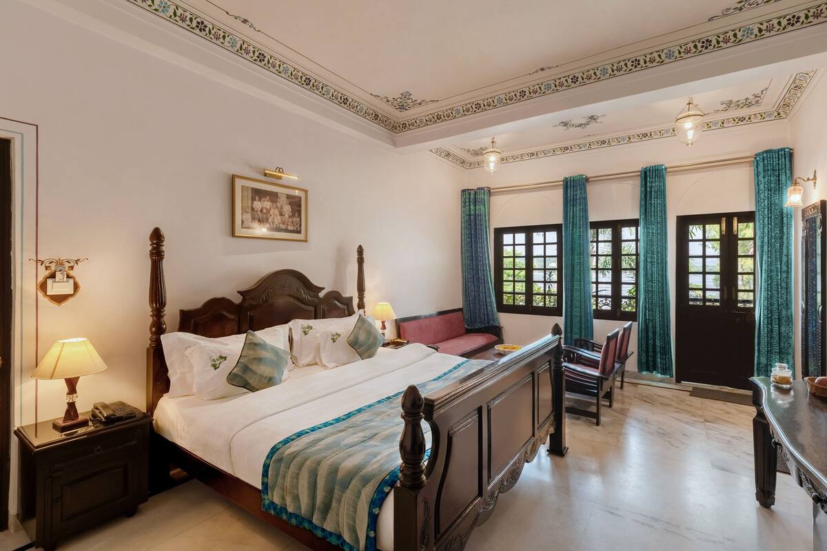 Une chambre à coucher de style traditionnel, avec un lit à baldaquin, une table de chevet avec une lampe, un tableau encadré au mur et une fenêtre avec des rideaux.