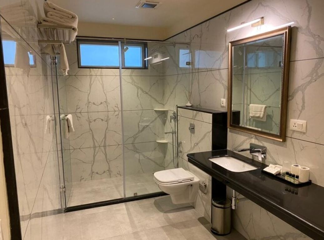Un baño moderno con ducha acristalada, inodoro, lavabo con encimera negra y espejo con marco dorado.