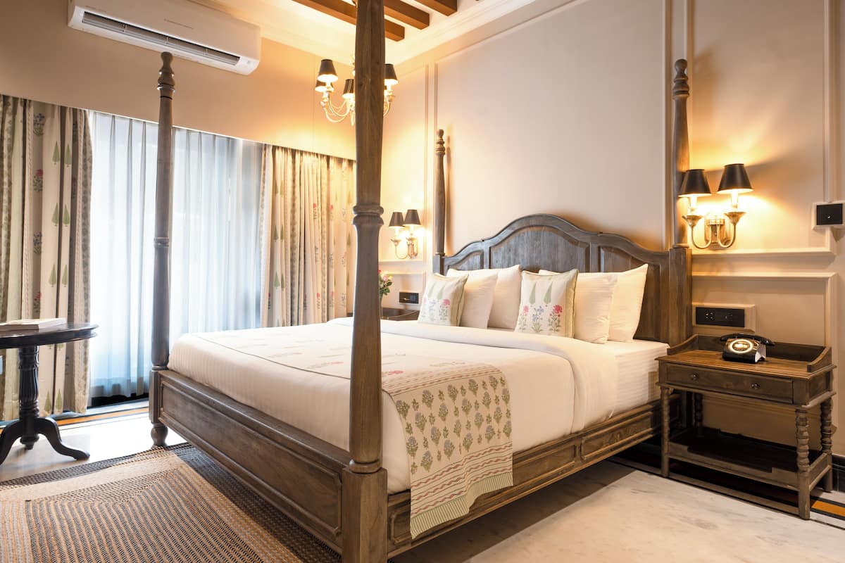 Un lit à baldaquin avec une tête de lit en bois, une table de chevet avec une lampe et une petite table de nuit avec un téléphone.