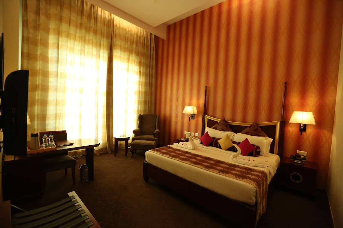 Ein Hotelzimmer mit einem Bett, zwei Nachttischlampen, einem Schreibtisch mit Stuhl, einem Fernseher und einem Klavier.