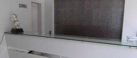 Un espace d’accueil avec un comptoir en verre, une statue équestre décorative, un panneau indiquant les services d’assistance aux voyageurs et un mur à texture.