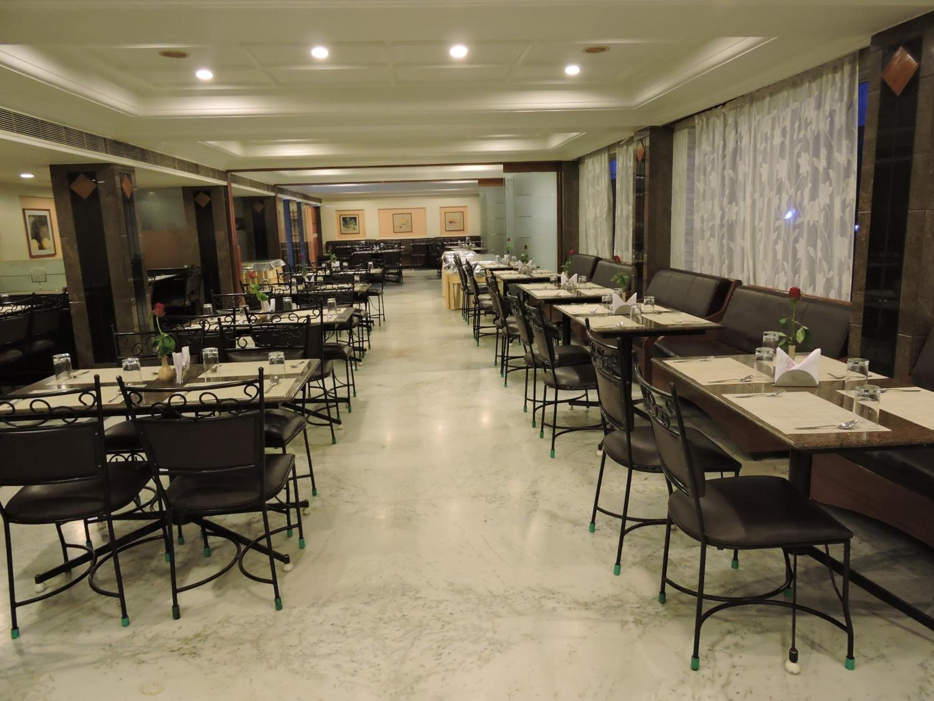 A spacious dining area with multiple tables and chairs, a marble floor, and a long counter with a cash register.