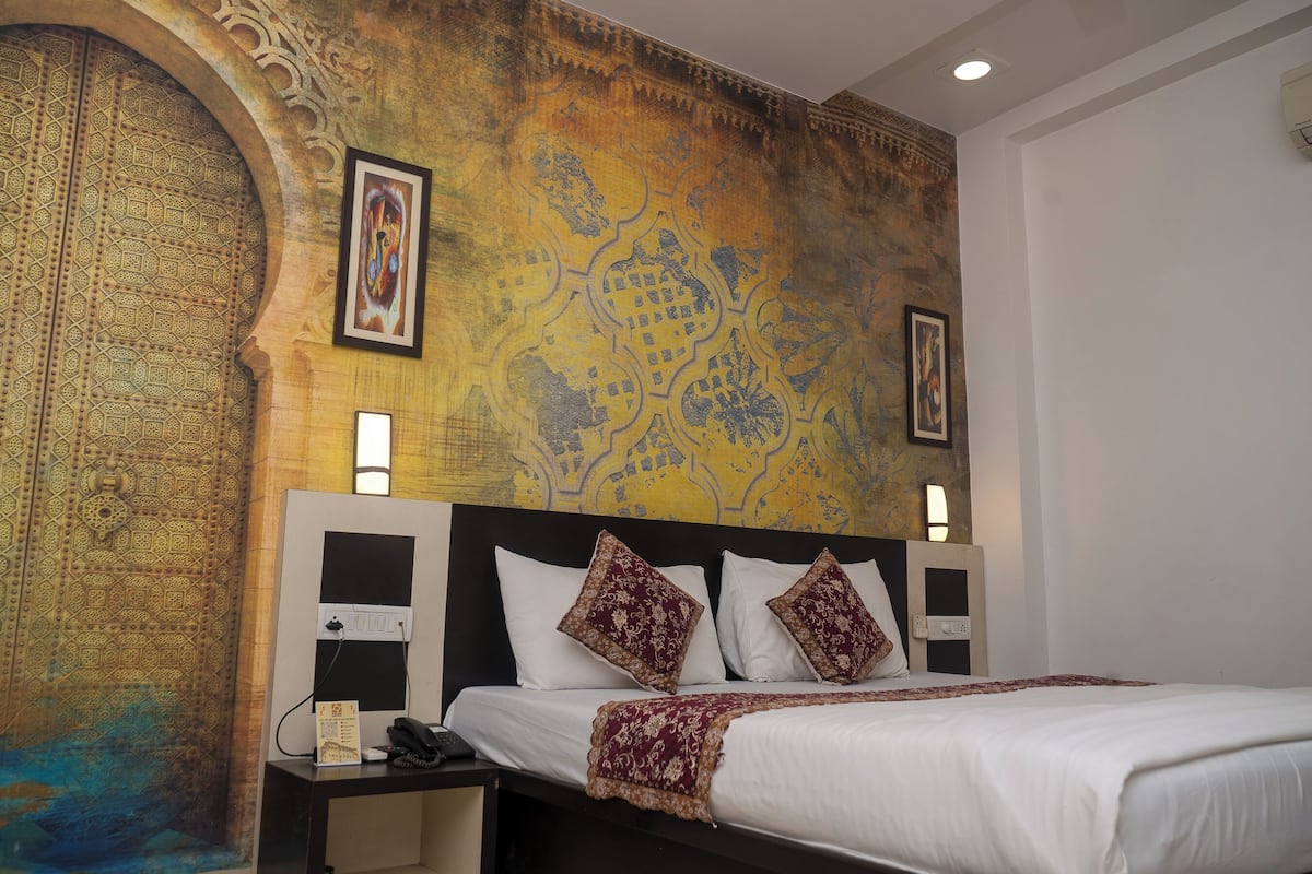 A hotel room with a large bed, a nightstand, a wall with intricate patterns, and a painting.