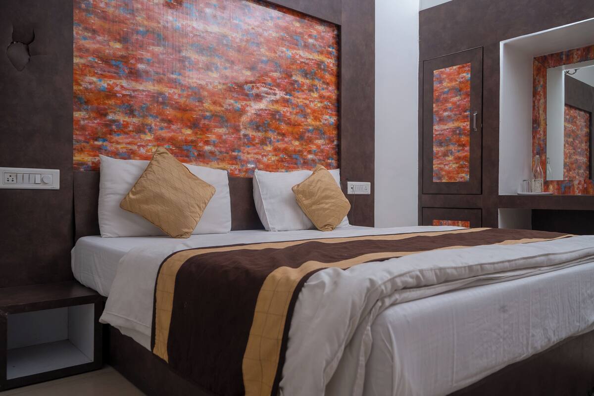 A modern hotel room with a large bed, a headboard with a colorful abstract painting, a bedside table, and a mirror.