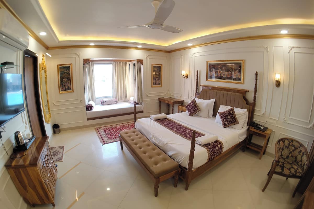 A spacious bedroom with a large bed, a bench, a TV, a desk, and a chair.