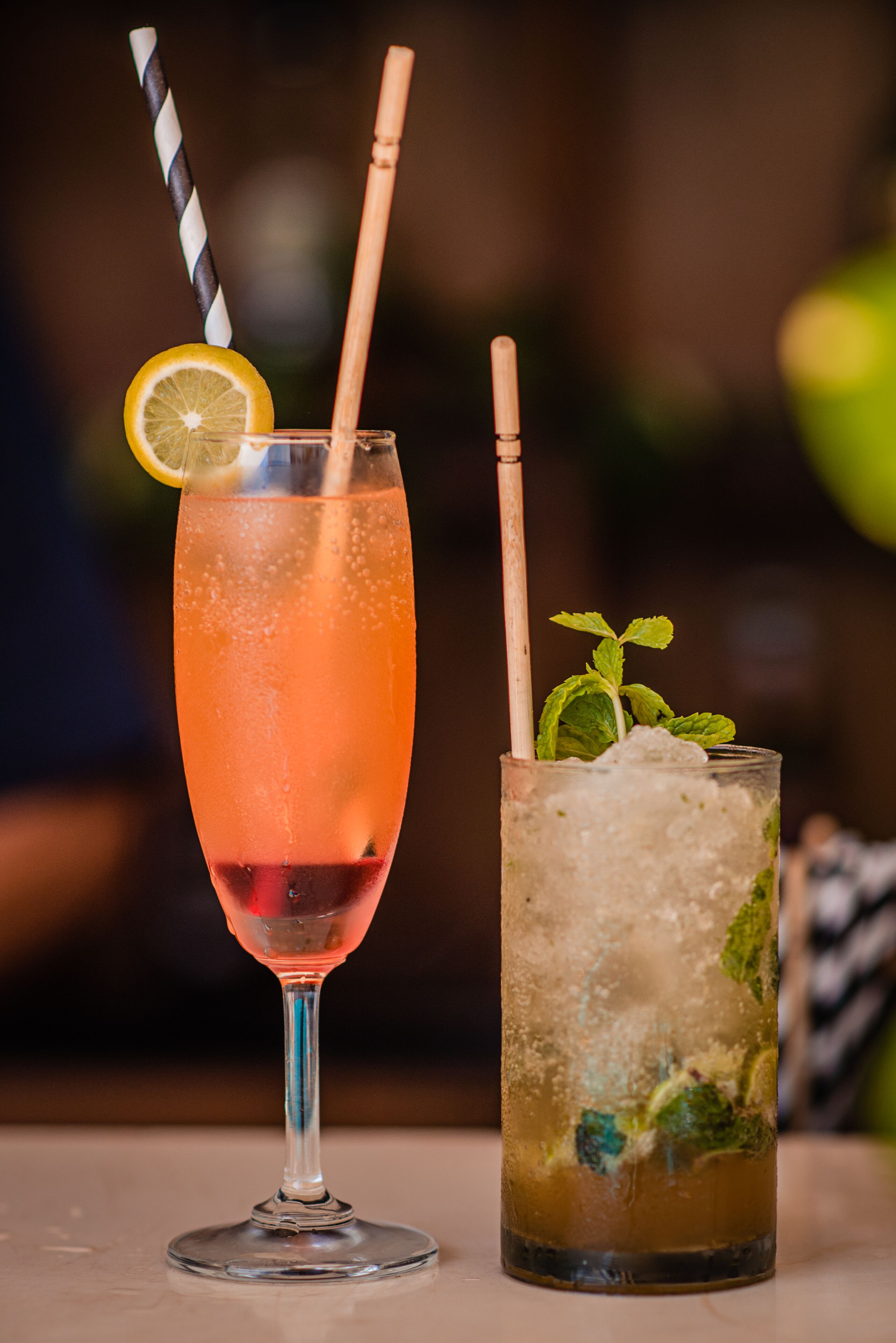 Two drinks in glasses, one with a lemon slice and mint, the other with ice and mint.