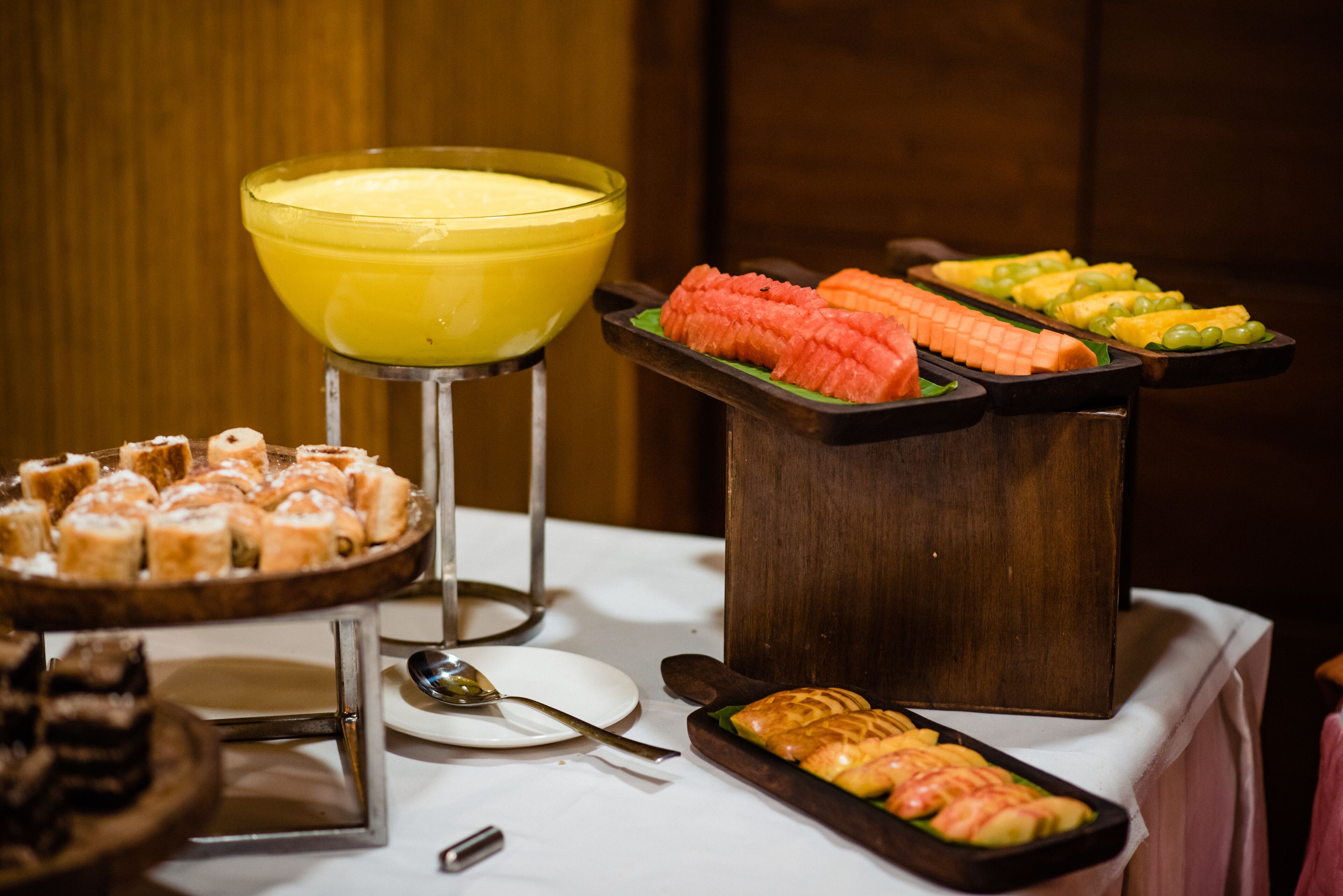 A buffet with various food items including sliced fruits, vegetables, and pastries.