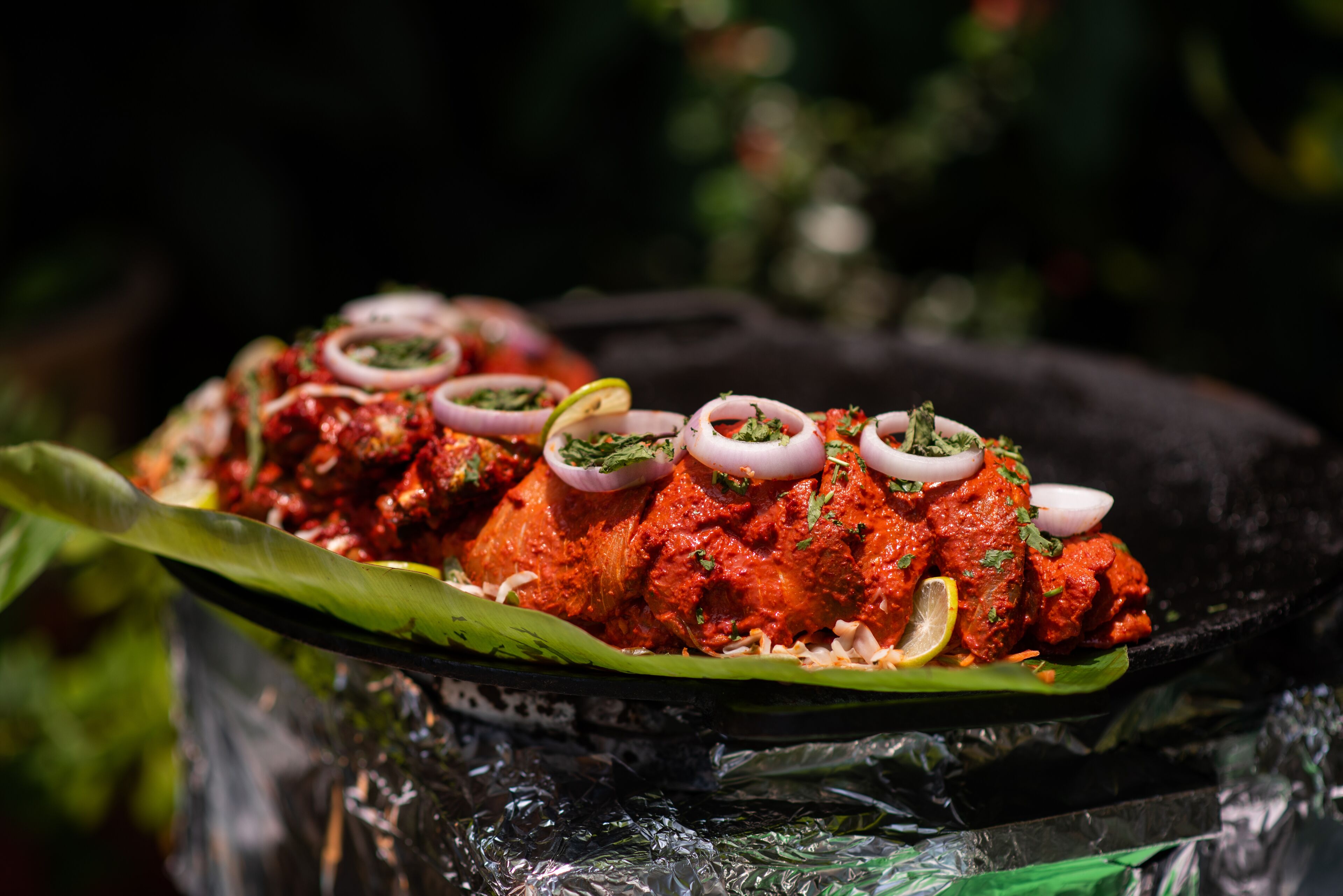 Un plato de pollo tandoori adornado con cebollas y rodajas de limón, servido sobre una hoja de plátano.
