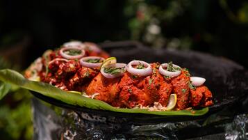 Un plato de pollo tandoori adornado con cebollas y rodajas de limón, servido sobre una hoja de plátano.