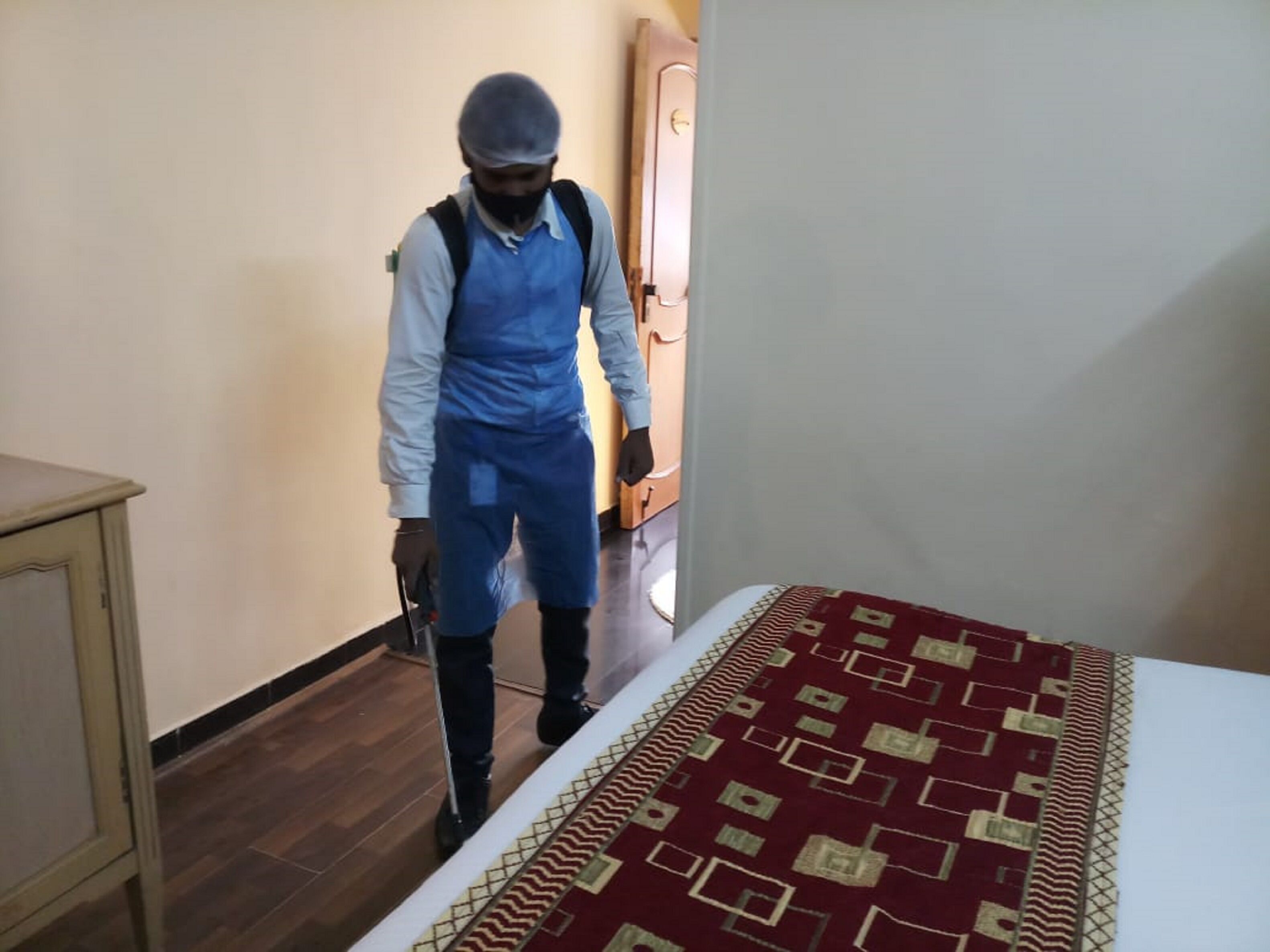 A person in a blue uniform cleaning a room with a patterned carpet and a wooden cabinet.
