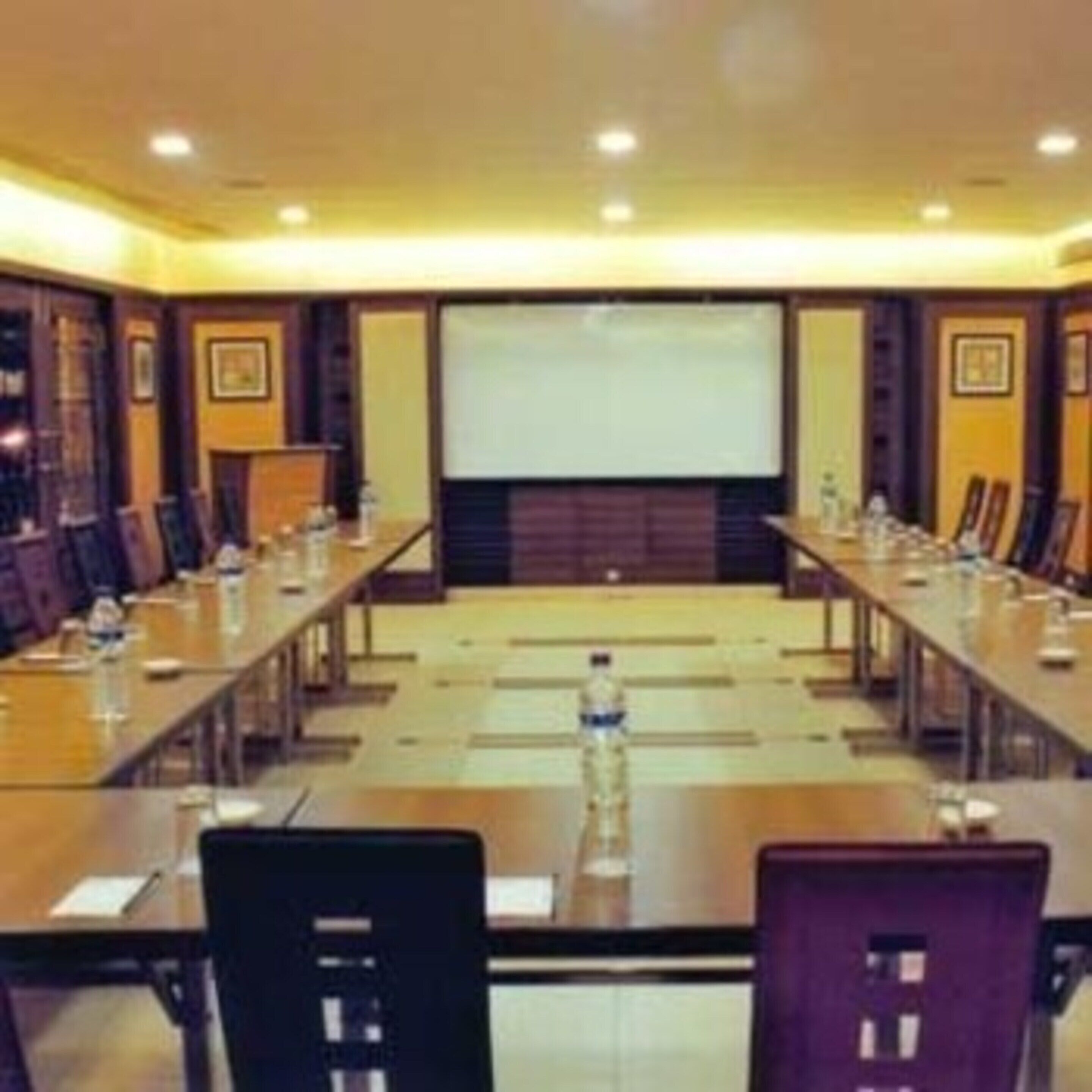 A conference room with a long table, chairs, a projector screen, and a podium.
