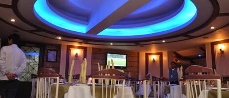 A restaurant with a circular ceiling design, tables with white tablecloths, and a television screen on the wall.
