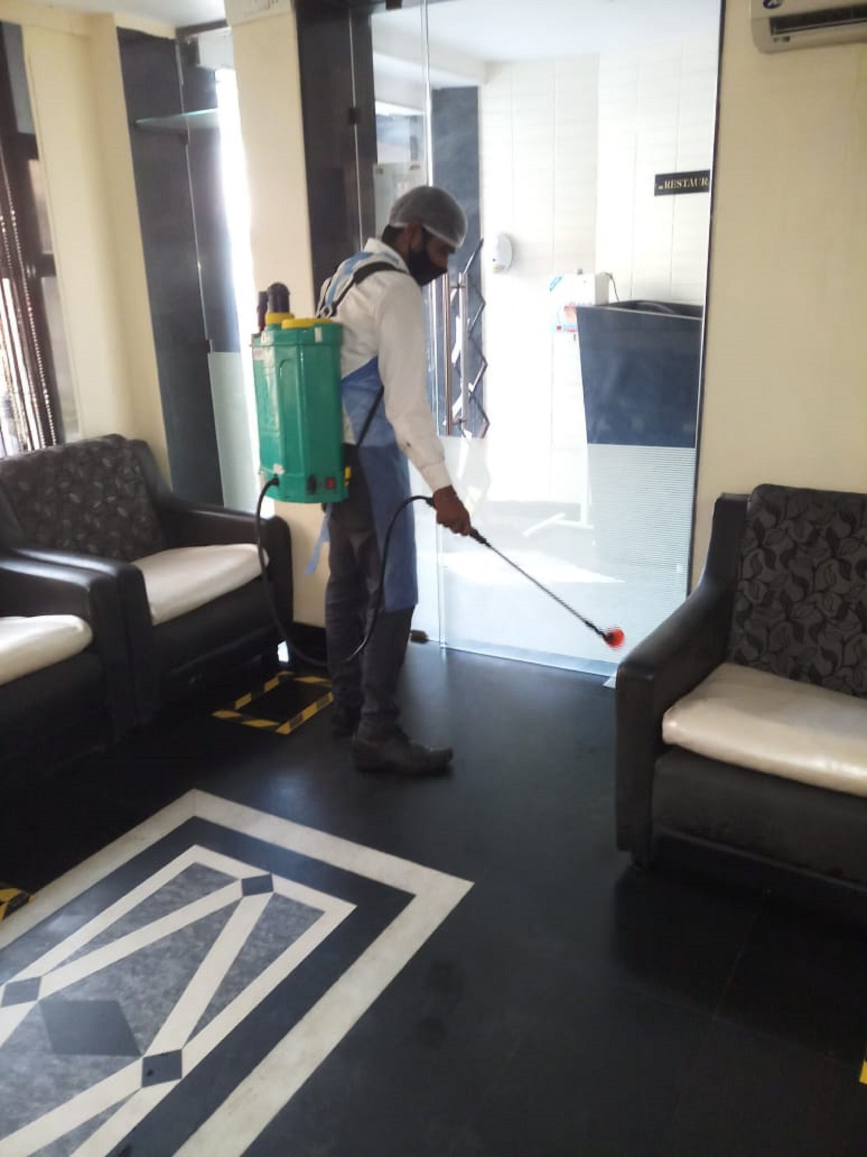 A person cleaning a lobby area with a spray bottle and a backpack.