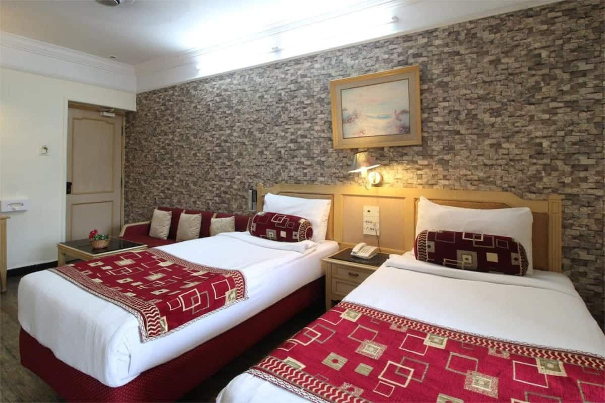 A hotel room with two beds, a stone wall, a painting, and a nightstand with a phone.