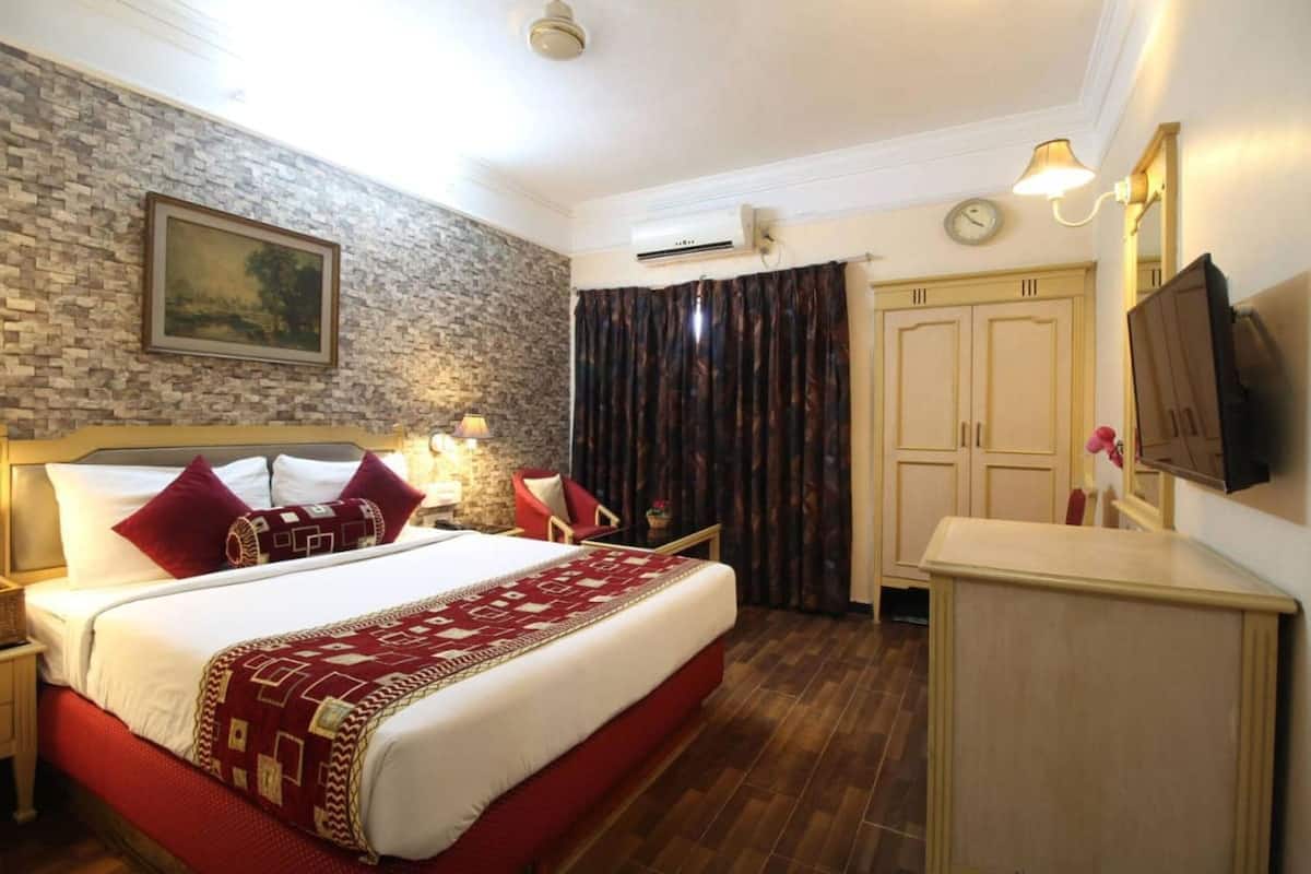 A hotel room with a bed, a desk, a chair, a television, and a clock on the wall.
