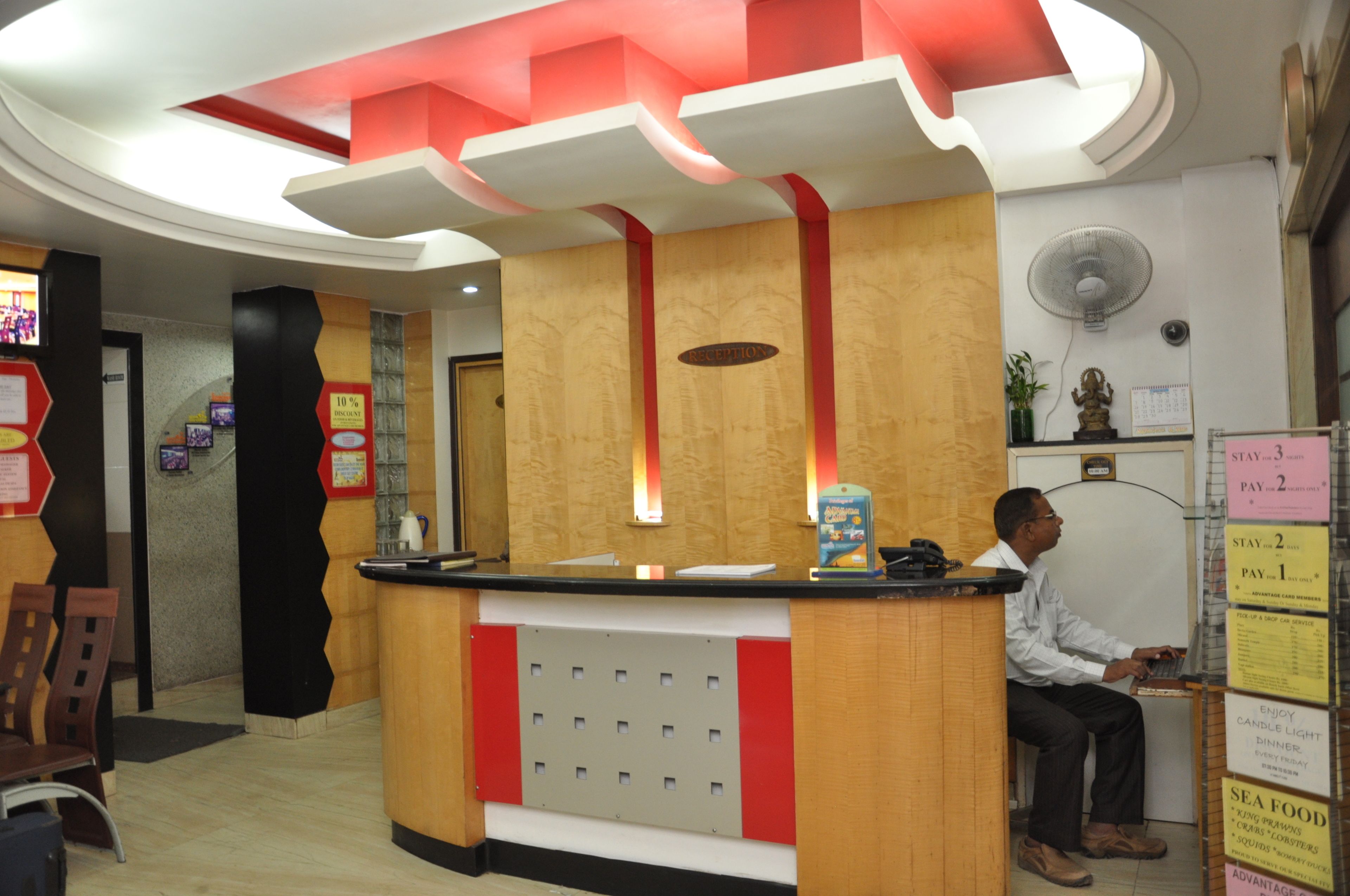 A reception desk with a wooden finish, a black counter, and a red accent wall. There is a fan on the wall and a calendar above it.