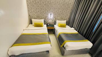 Habitación de hotel con dos camas individuales, cada una con cubrecama gris y blanco, un cojín de color amarillo y una mesita de noche con lámpara.
