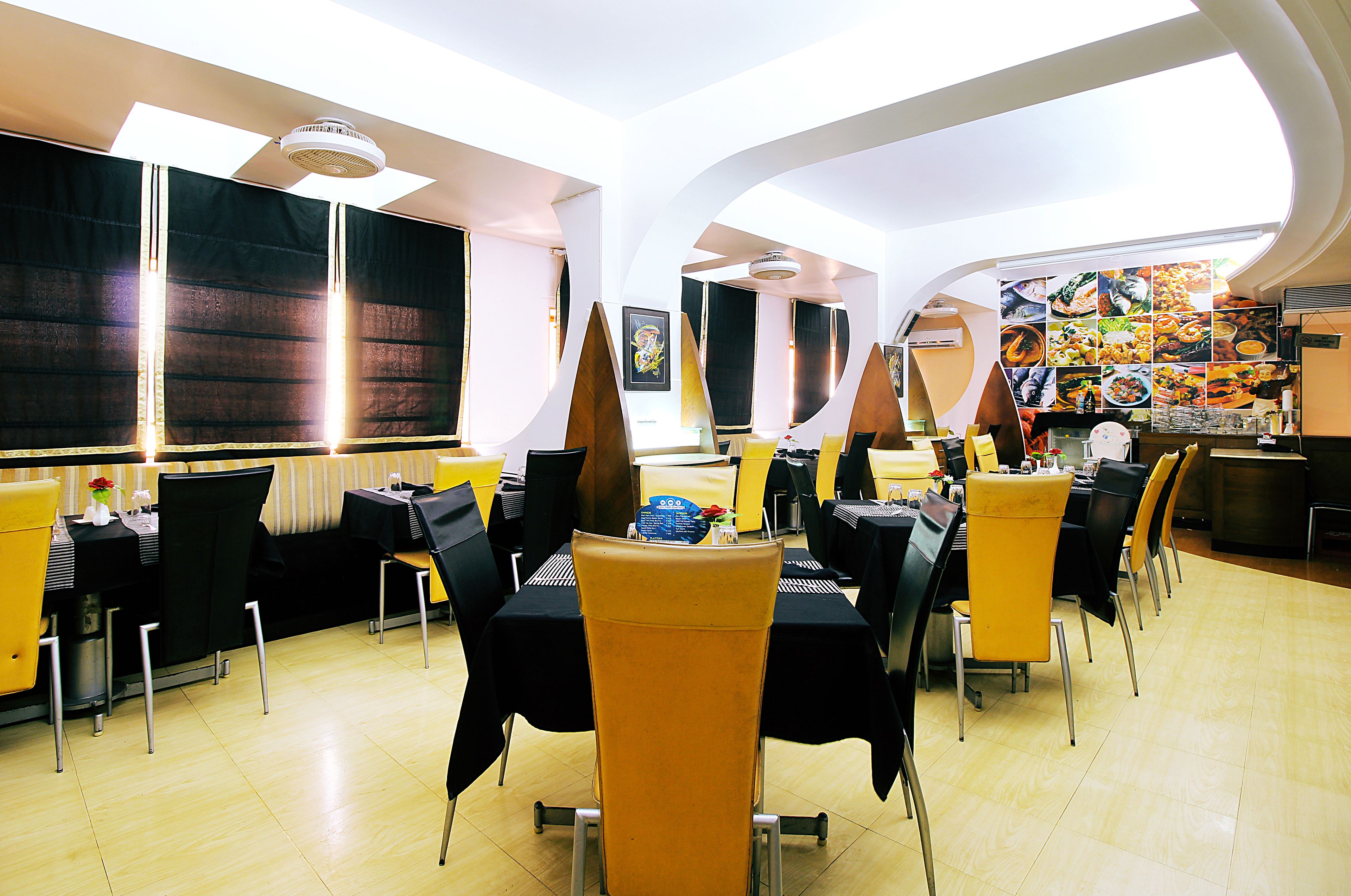 Un restaurante con mesas y sillas altas, un mural grande en la pared y un techo luminoso.