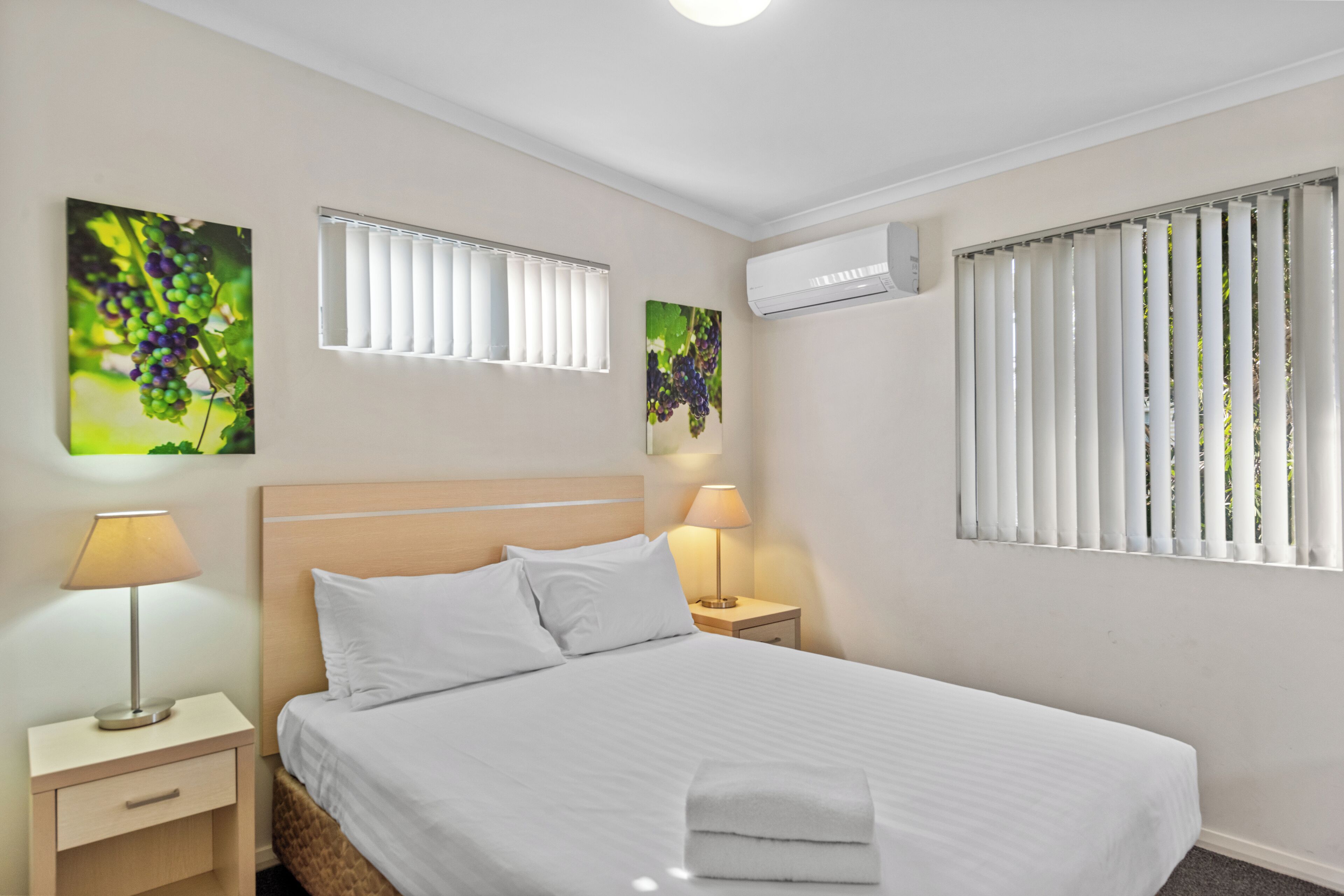 A hotel room with a large bed, two bedside tables with lamps, a window with blinds, and wall art.