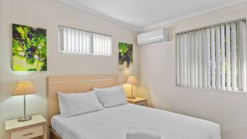A hotel room with a large bed, two bedside tables with lamps, a window with blinds, and wall art.