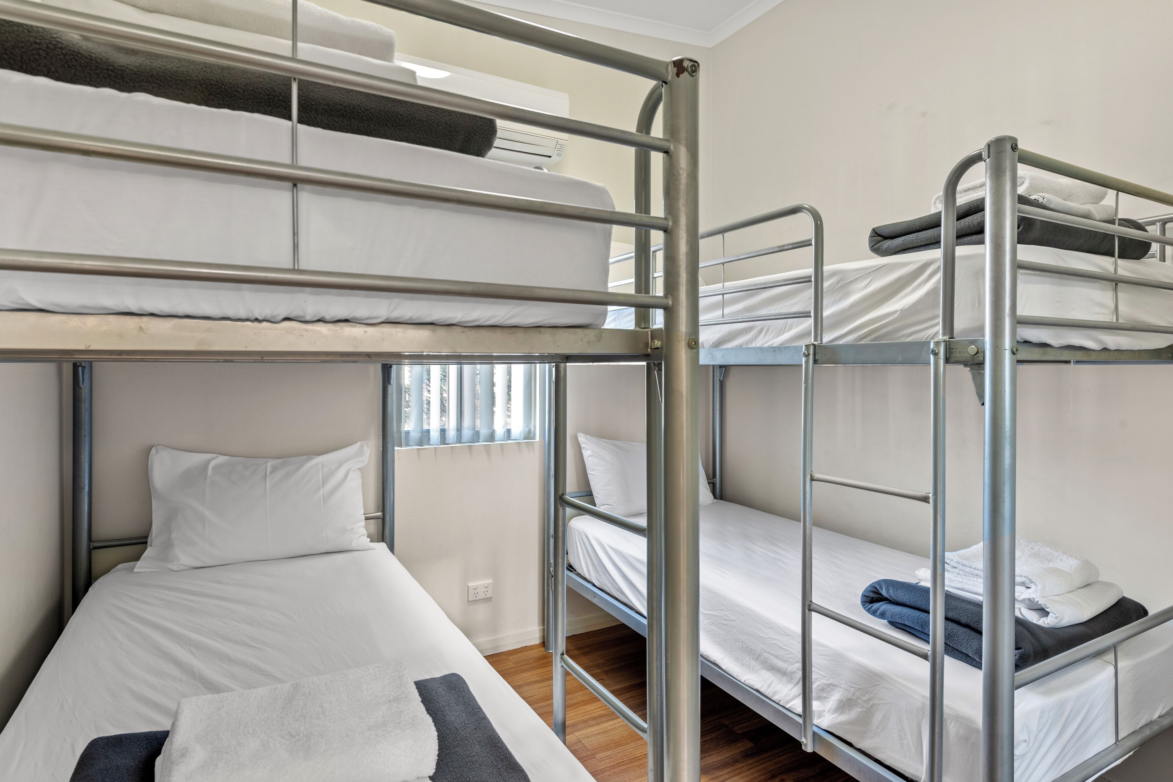 A bunk bed room with a window, a power outlet, and a wooden floor.