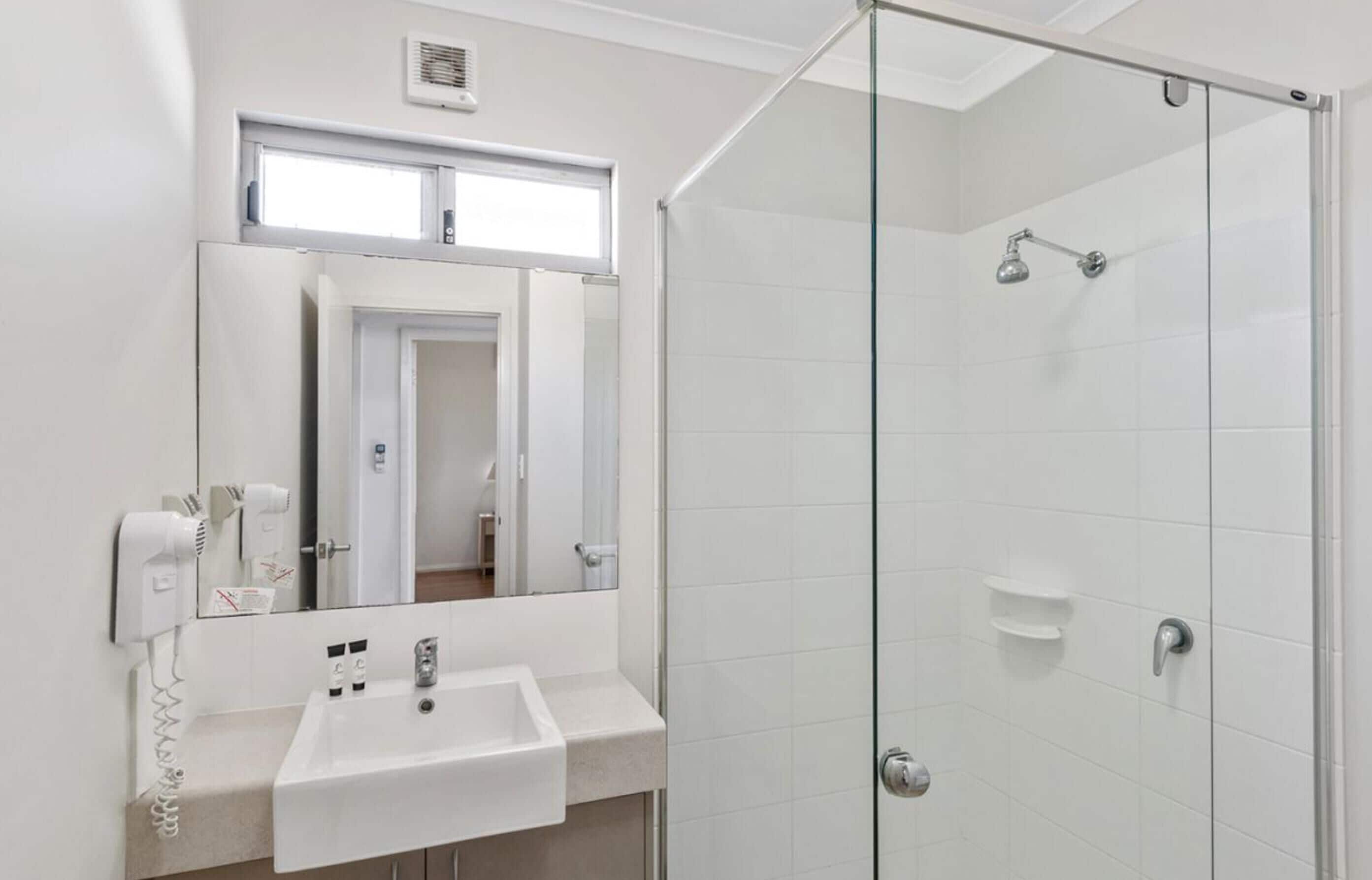A modern bathroom with a glass-enclosed shower, a sink with a mirror above, and a hairdryer mounted on the wall.