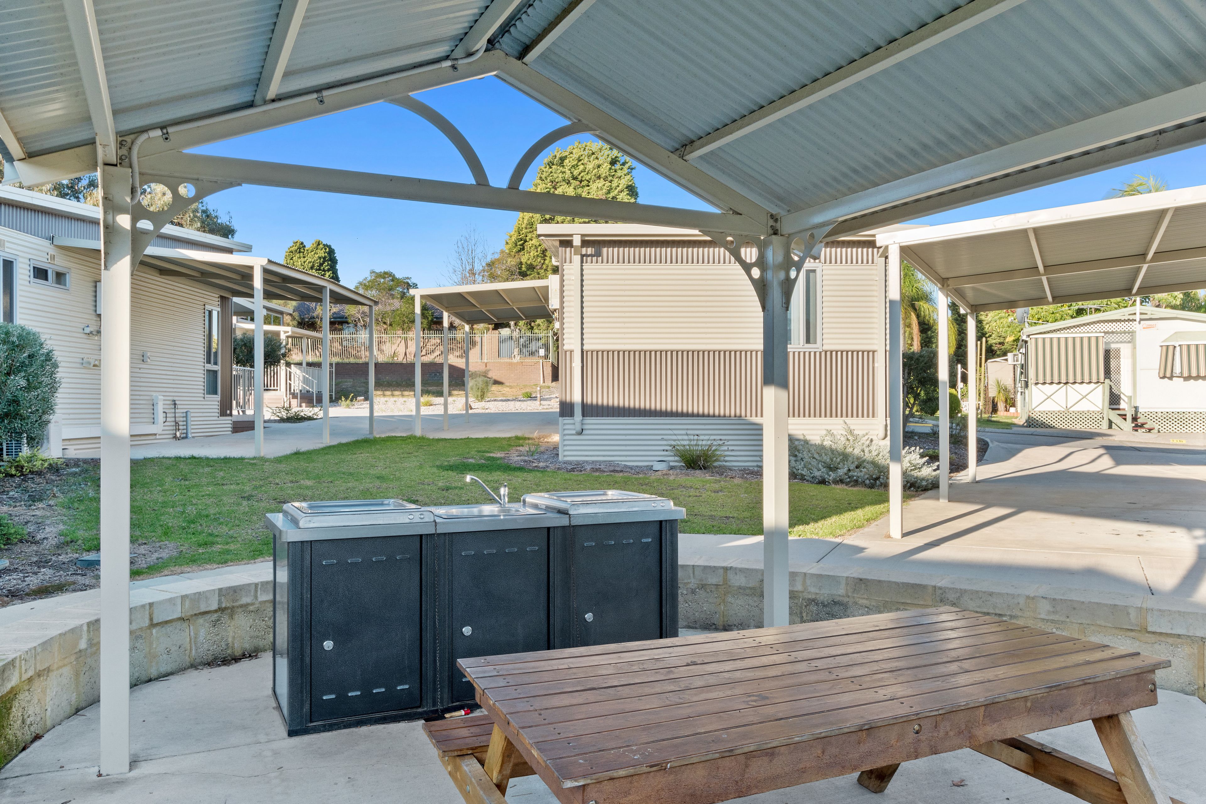 A covered outdoor area with a picnic table and a barbecue grill.