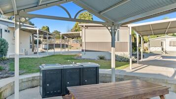 A covered outdoor area with a picnic table and a barbecue grill.