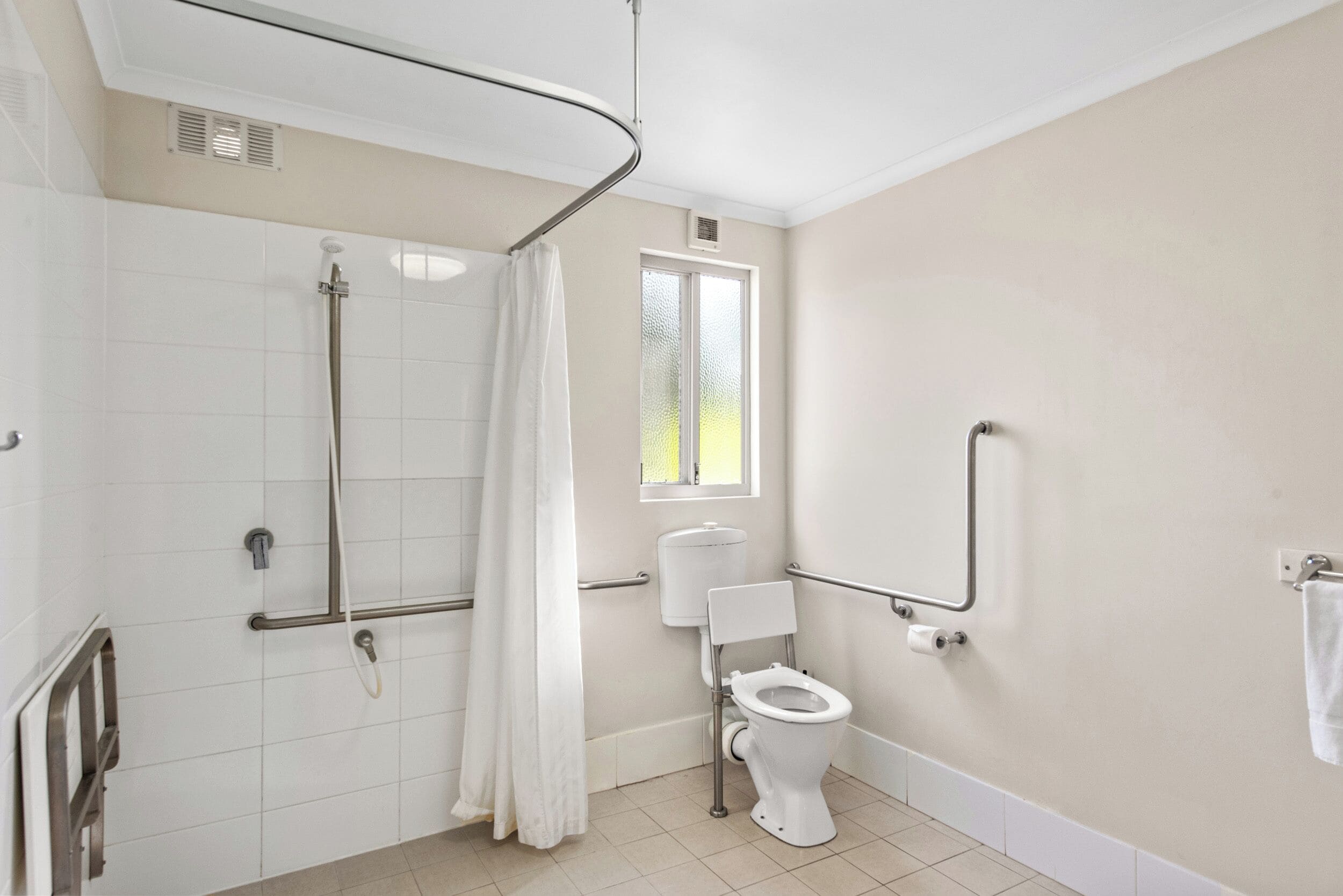 A bathroom with a shower, toilet, and grab bars.