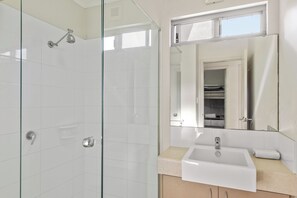 Une salle de bain moderne avec une douche à parois de verre, un lavabo blanc et un miroir au-dessus.