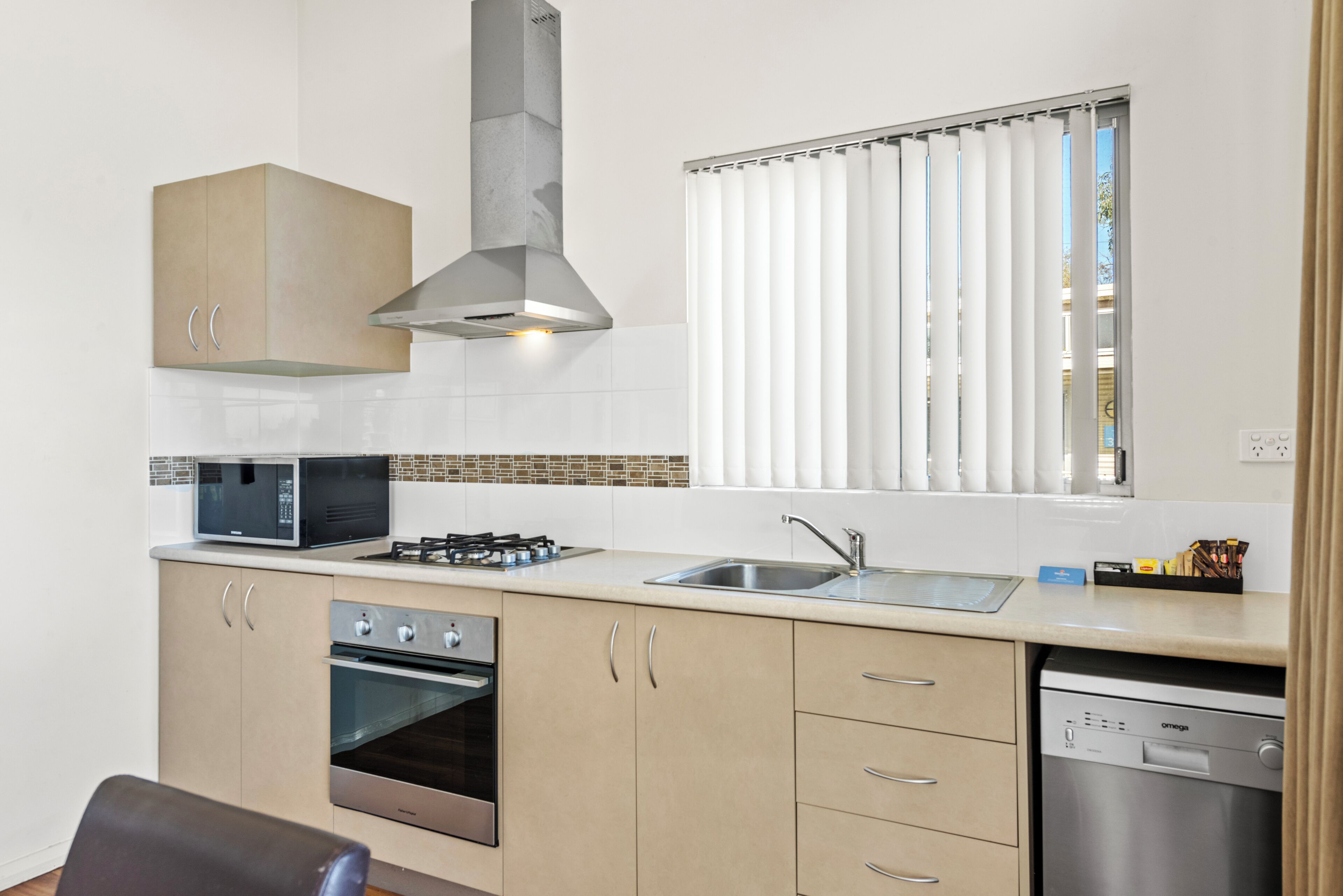 A modern kitchen with a microwave, stove, oven, dishwasher, and a window with blinds.