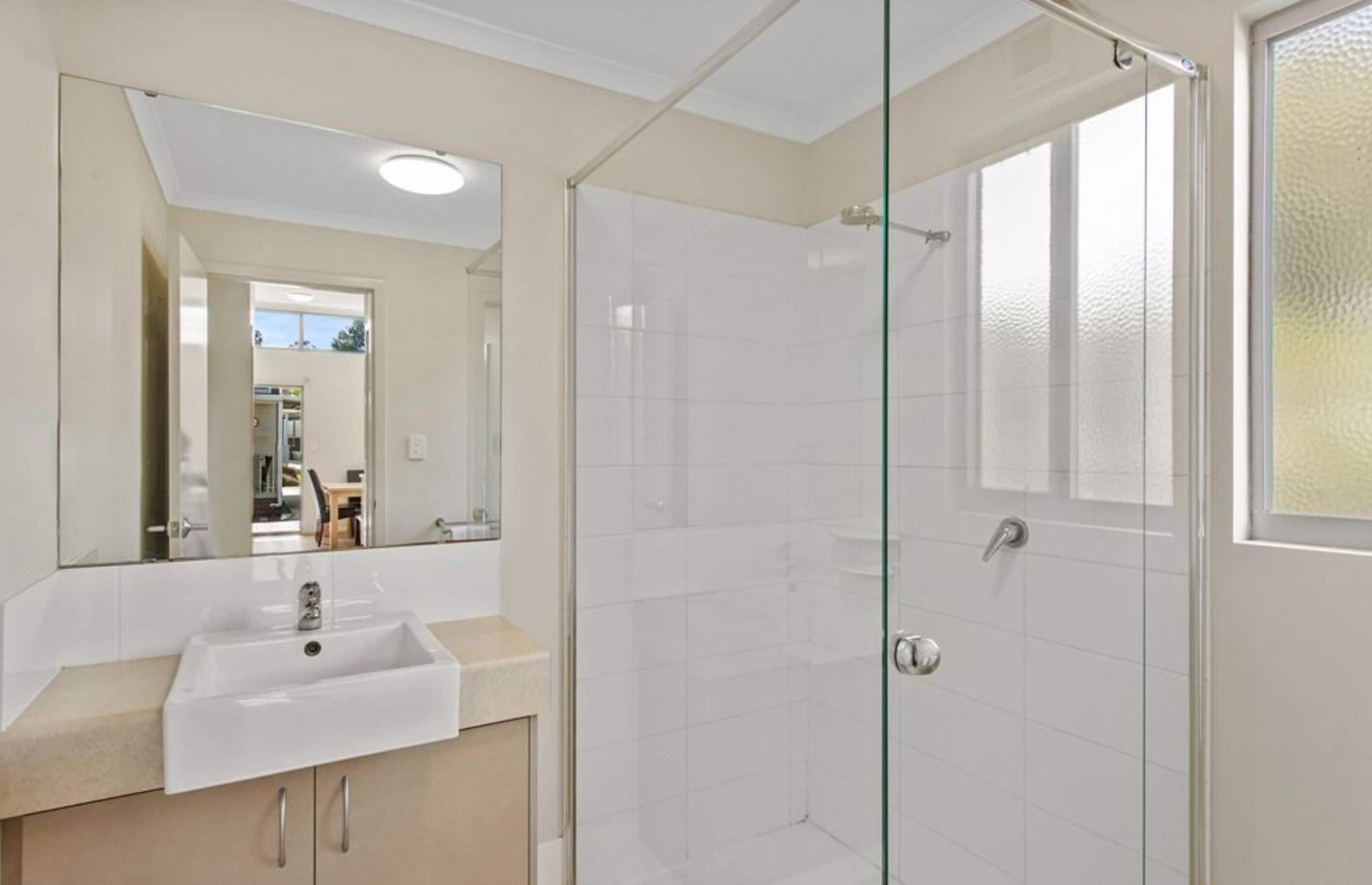 A bathroom with a glass shower enclosure, a sink, and a mirror.