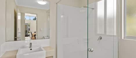 A bathroom with a glass shower enclosure, a sink, and a mirror.