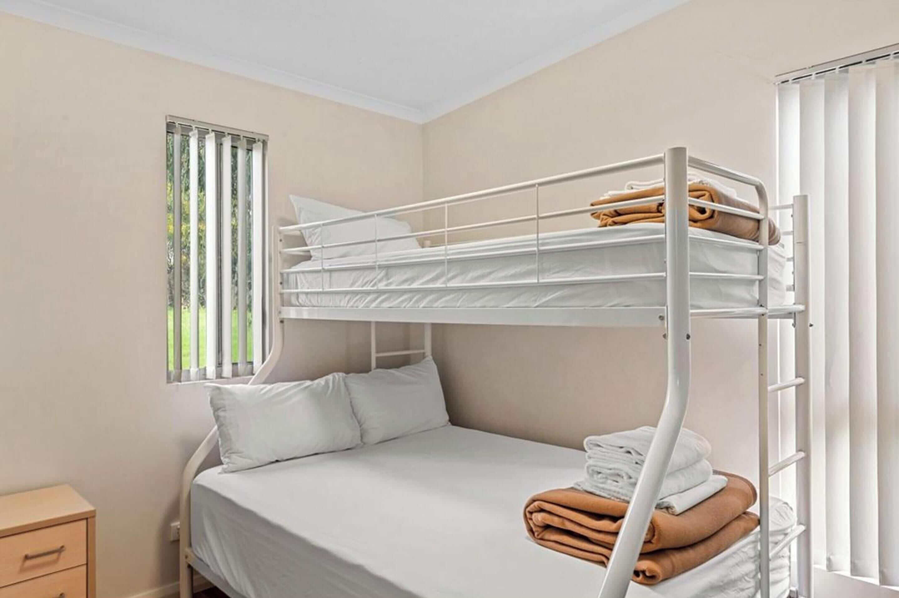 A bunk bed room with a window, a bedside table, and a neatly made bed.