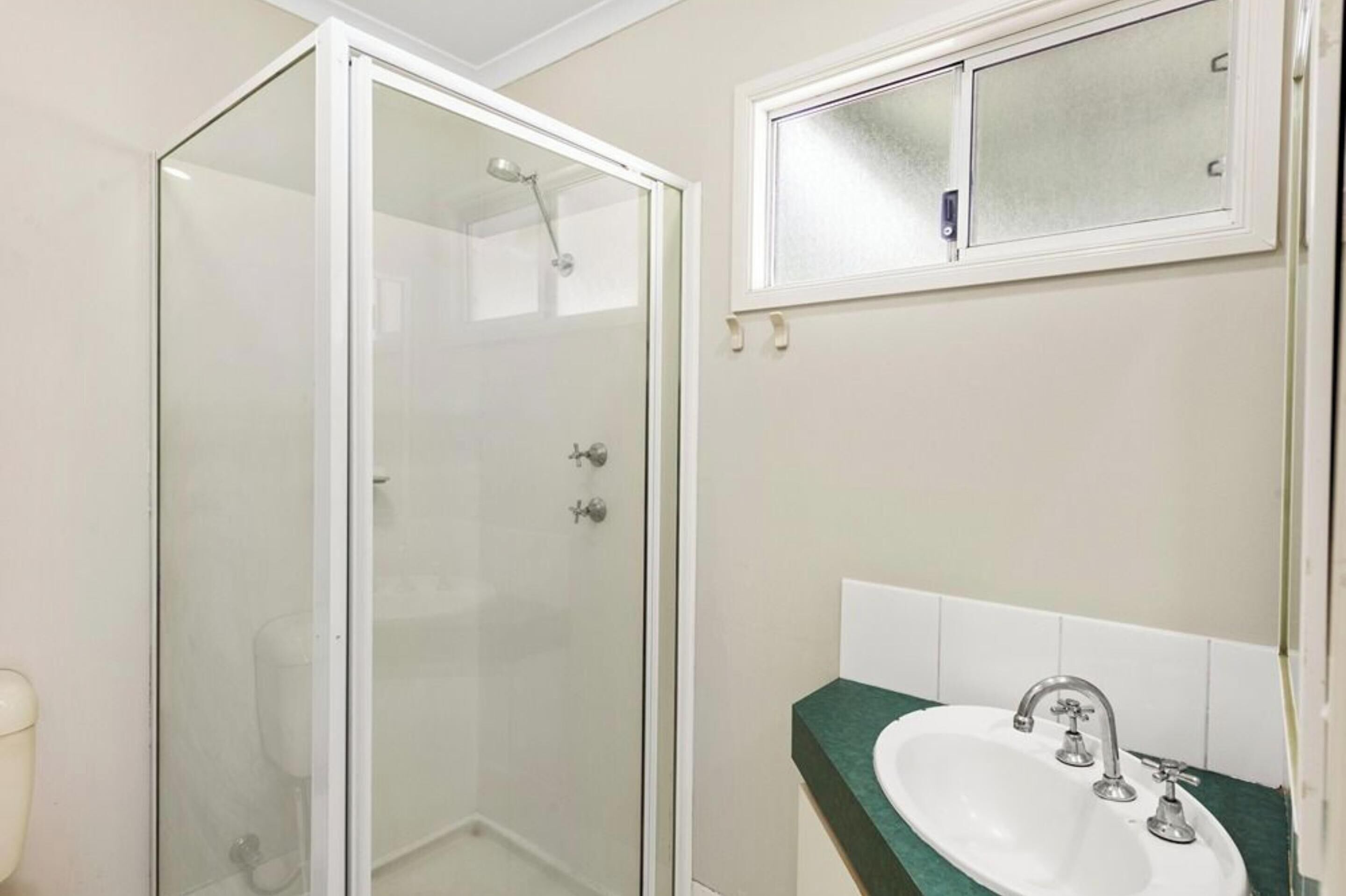 Une salle de bain avec une douche à parois de verre, un lavabo doté d’un plan de travail vert et un miroir au-dessus du lavabo.